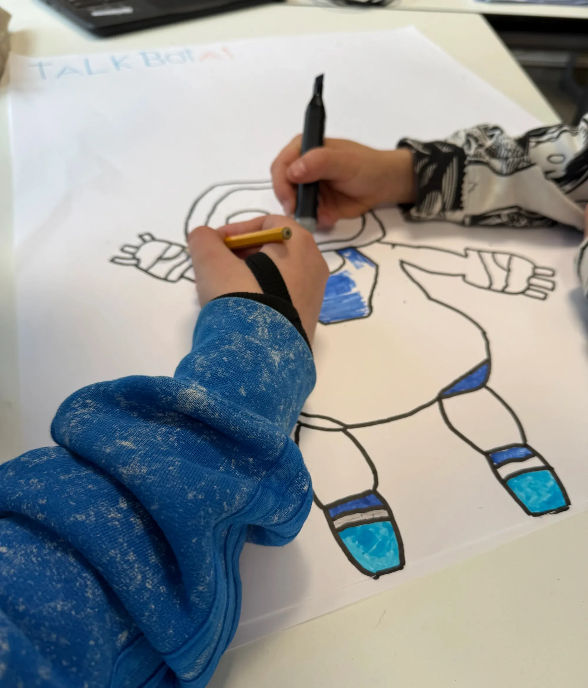 Two workshop participants colouring in a robot of their design called 'TalkBotAI'