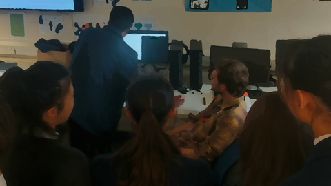 A blurred photograph of Rayo and some high school students looking at something on a computer screen